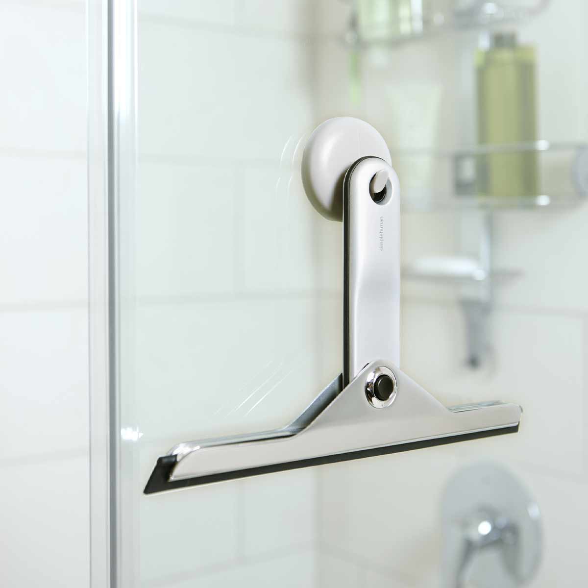 Simplehuman Foldaway Squeegee, Polished Stainless Steel, mounted on shower glass with suction cup storage.