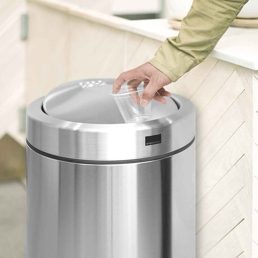 Detail view of Simplehuman 55L Swing Top Can in Brushed Stainless Steel, showing hand disposing trash through the swing lid.