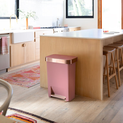 Lifestyle view of Simplehuman 45L Hybrid Step Can, Dusty Rose/Rose Gold, placed by a modern kitchen island.