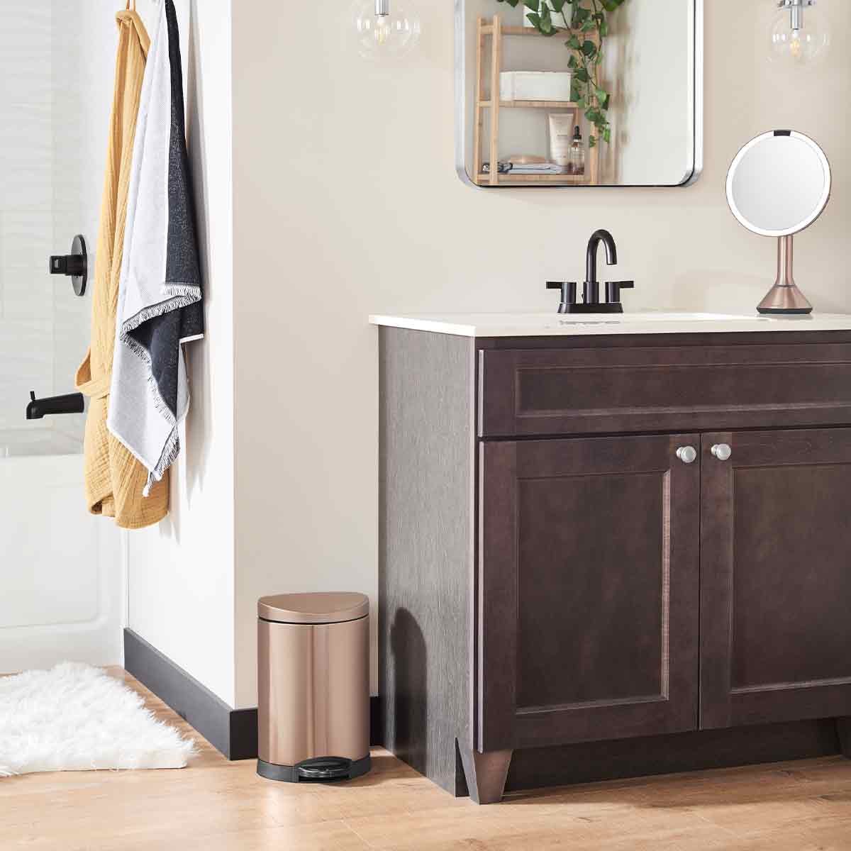 Simplehuman 6L Semi-Round Step Can in Rose Gold, used next to a bathroom vanity, hands-free step pedal.