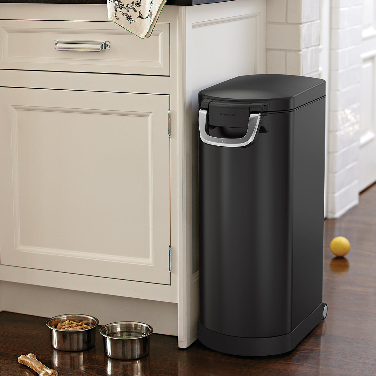 Kitchen view, Simplehuman X-Large Pet Food Can, Matte Black, next to pet bowls. Airtight locking handle ensures fresh storage, features mobility wheels.