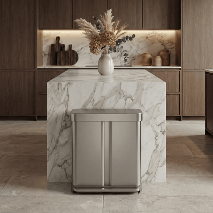 Simplehuman's 58L Step Recycler in brushed in a modern, luxury lived in home. The background features wooden cabinets, plants on a marble counter top and other counter appliances.