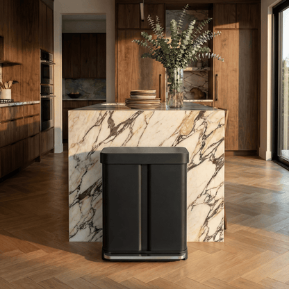 Simplehuman's 58L Step Recycler in Brushed featuring a marble counter top with plants and dishes on top and wooden cabinets in the background with warmer mood lighting.