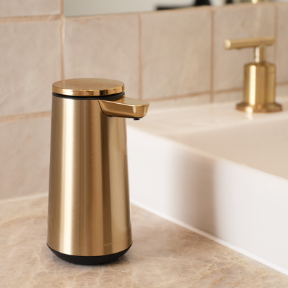 Angled view of Simplehuman Brushed Brass Sensor Pump Foam next to a sink with a matching faucet, touch-free operation.